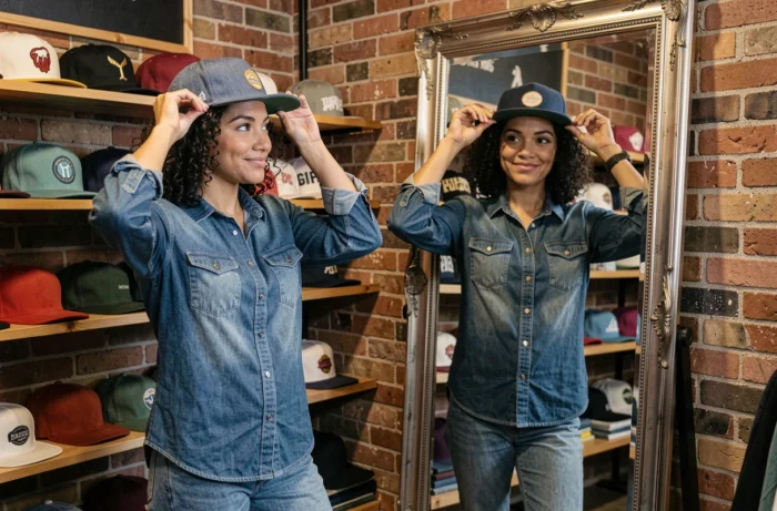 Femme essayant différentes casquettes devant un miroir dans une boutique de vêtements pour trouver la bonne taille